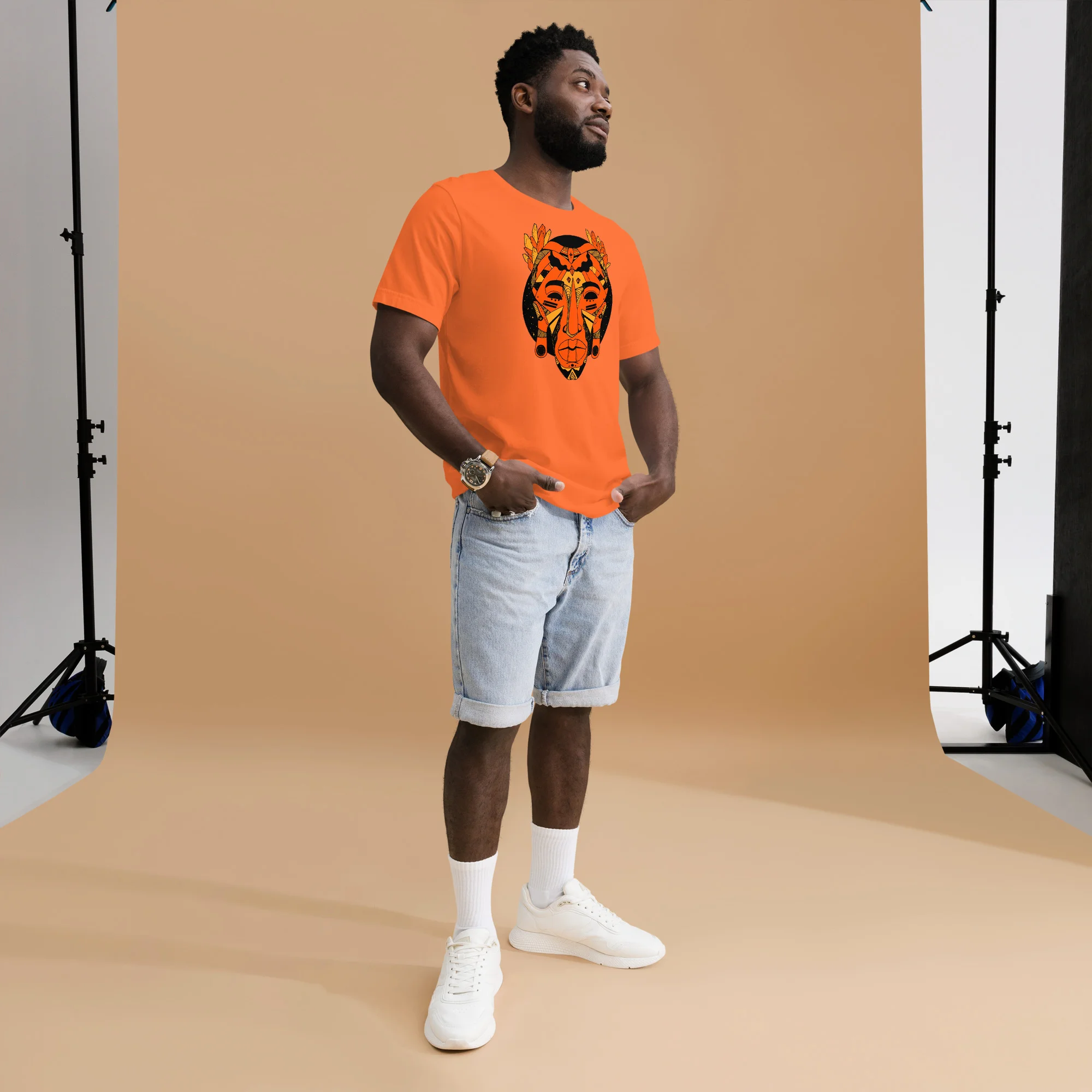 Man wearing orange African mask t-shirt with black graphic design and light denim shorts