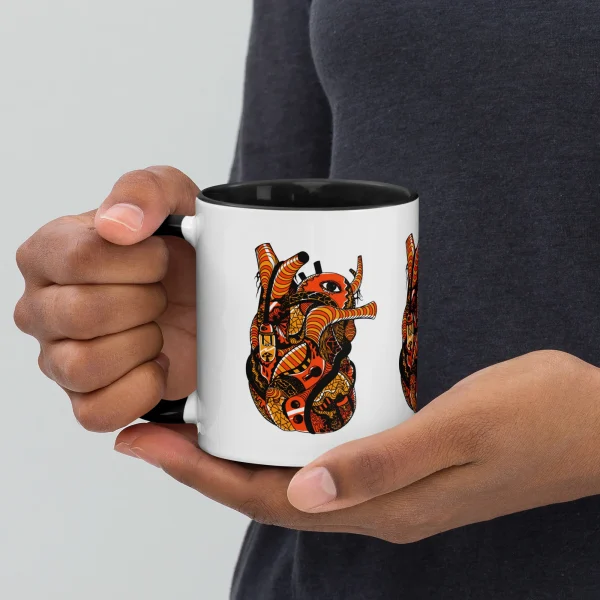 Person holding white anatomical heart coffee mug with black interior and orange gothic design