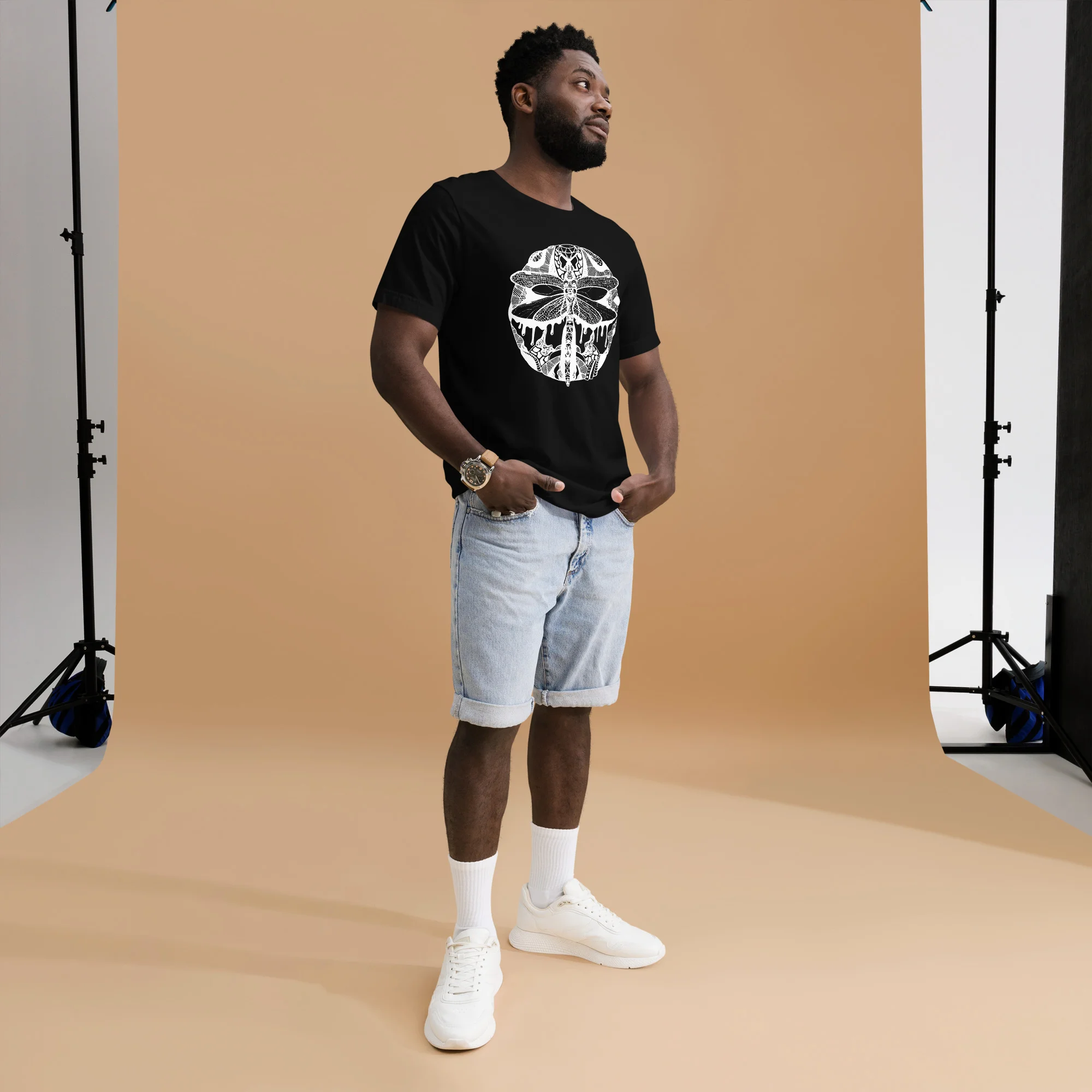 Man wearing black dragonfly t-shirt with white circle line art design, styled with light denim shorts.