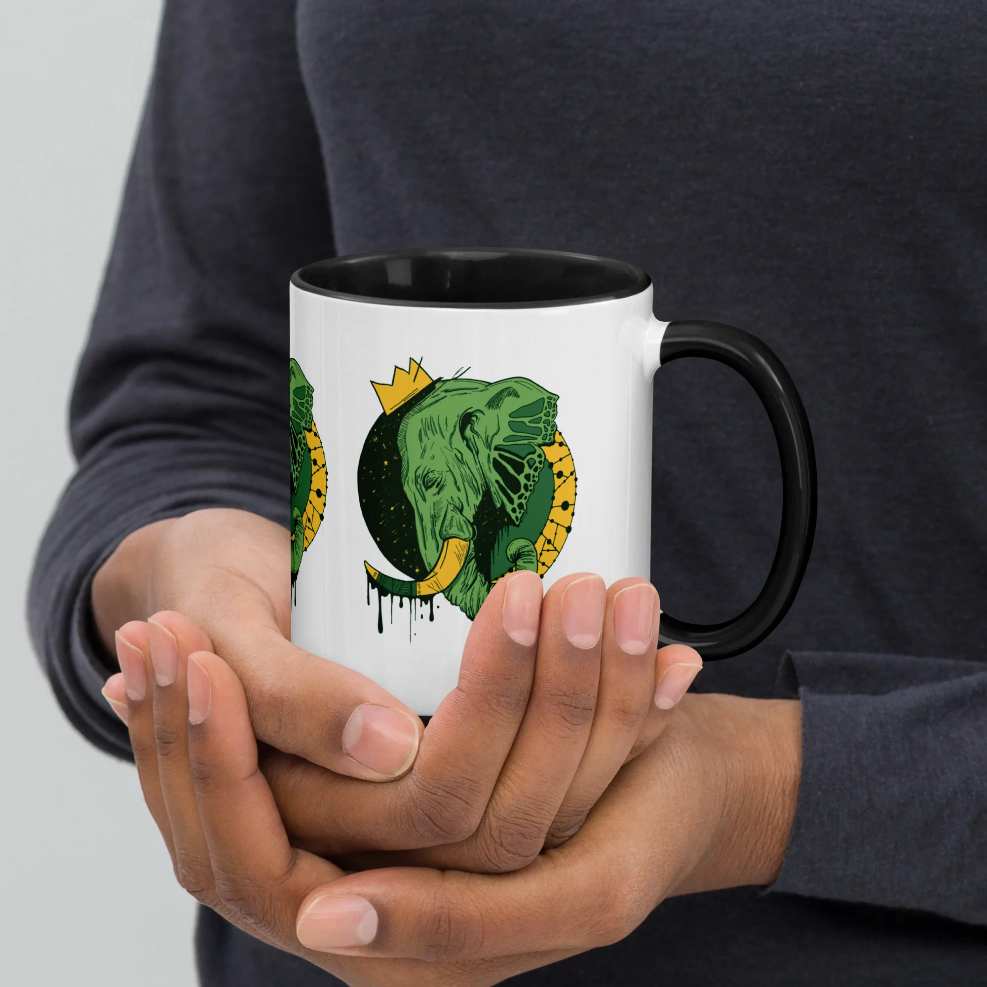 Person holding white ceramic elephant mug with green royal elephant art and black interior, featuring bold crown illustration