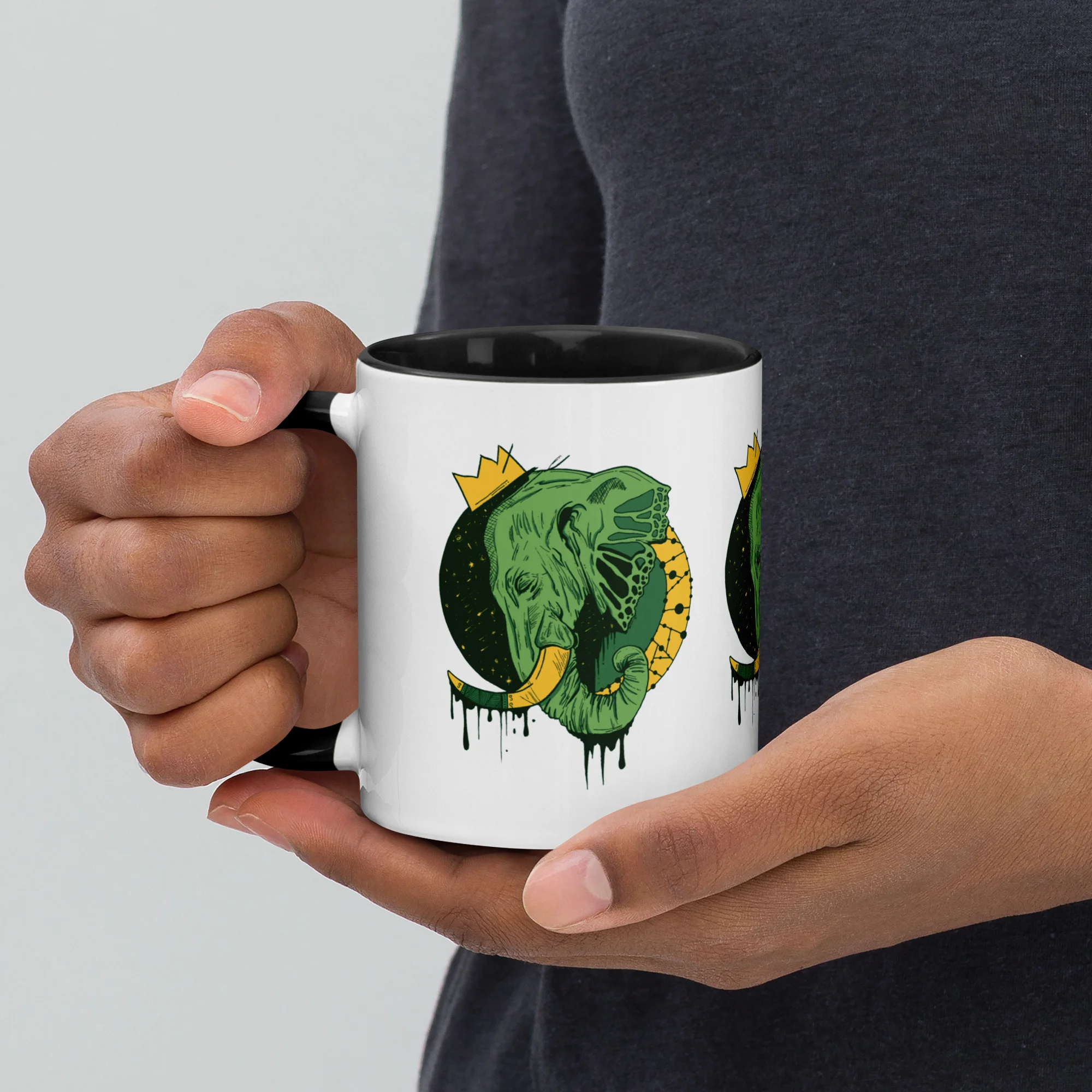 Person holding white ceramic elephant mug with green royal elephant illustration and gold crown design