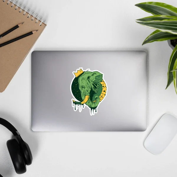 Green crowned elephant sticker with gold accents on silver laptop lid surrounded by desk workspace