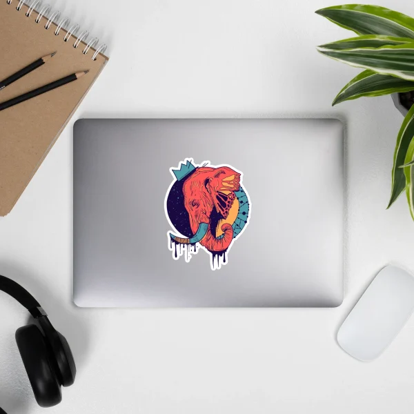 Royal coral and teal crowned elephant sticker displayed on a silver laptop in a creative workspace