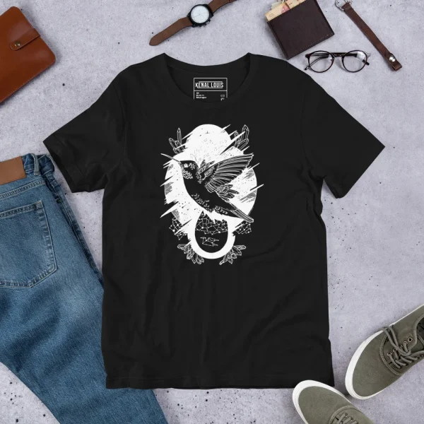 Black hummingbird t-shirt featuring white line art design with moon and botanical elements, displayed flat lay with accessories