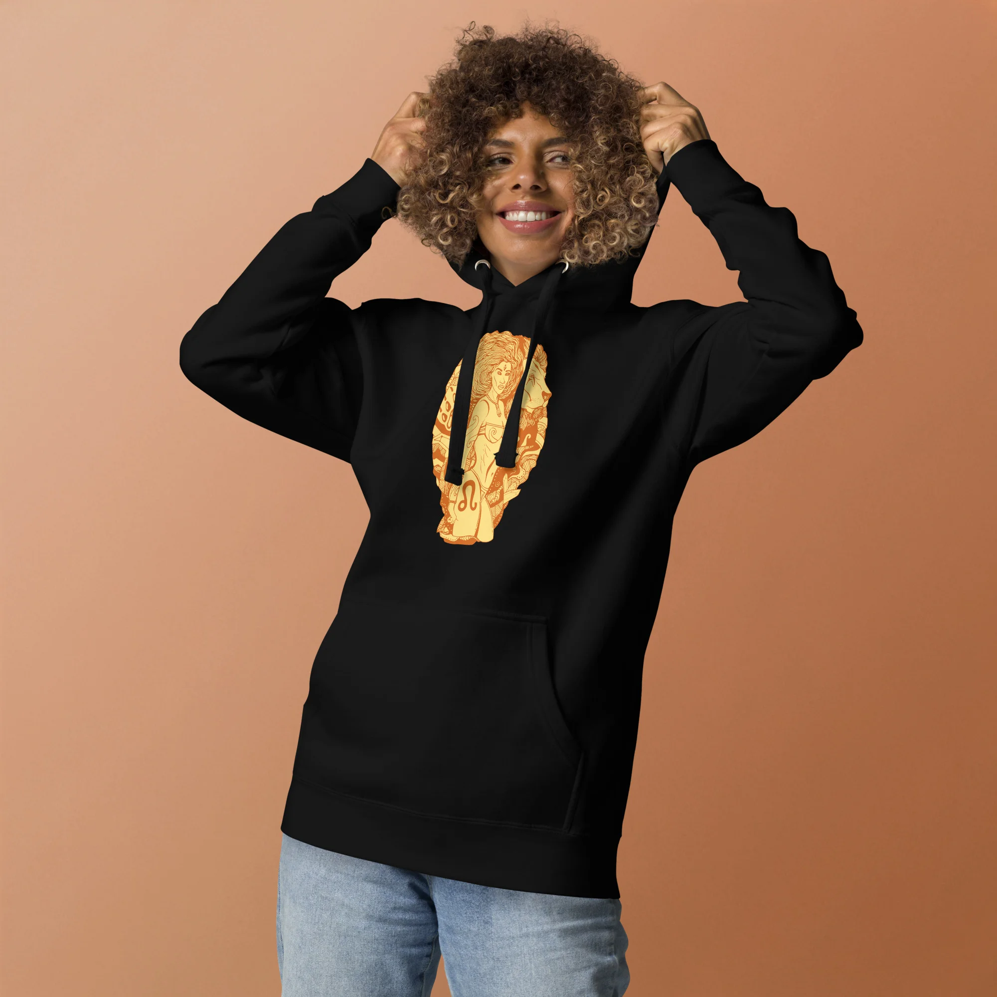 Black leo hoodie with gold zodiac artwork worn by model with curly hair against terracotta background