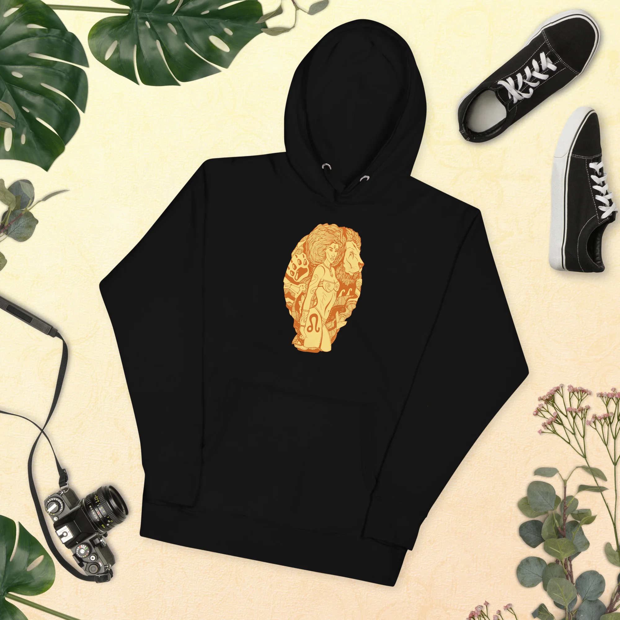 Black leo hoodie with terracotta zodiac artwork on chest, displayed flat lay with sneakers and accessories