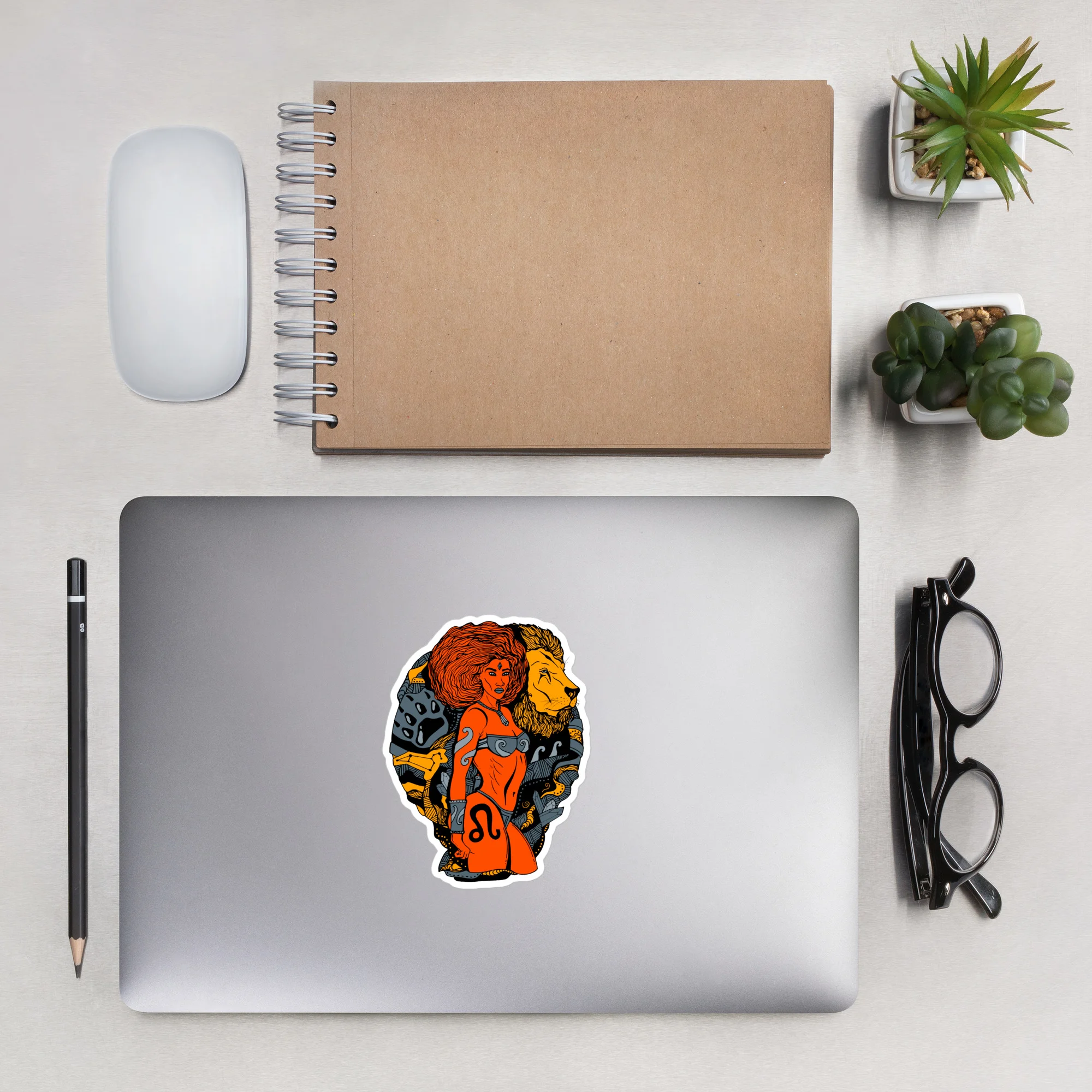 Grey and orange Leo sticker with Amazonian warrior design on silver laptop, featuring bold vinyl artwork