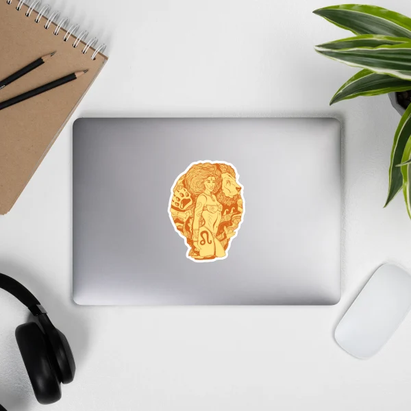Terracotta Leo sticker with warrior design on silver laptop, surrounded by workspace accessories and green plant.