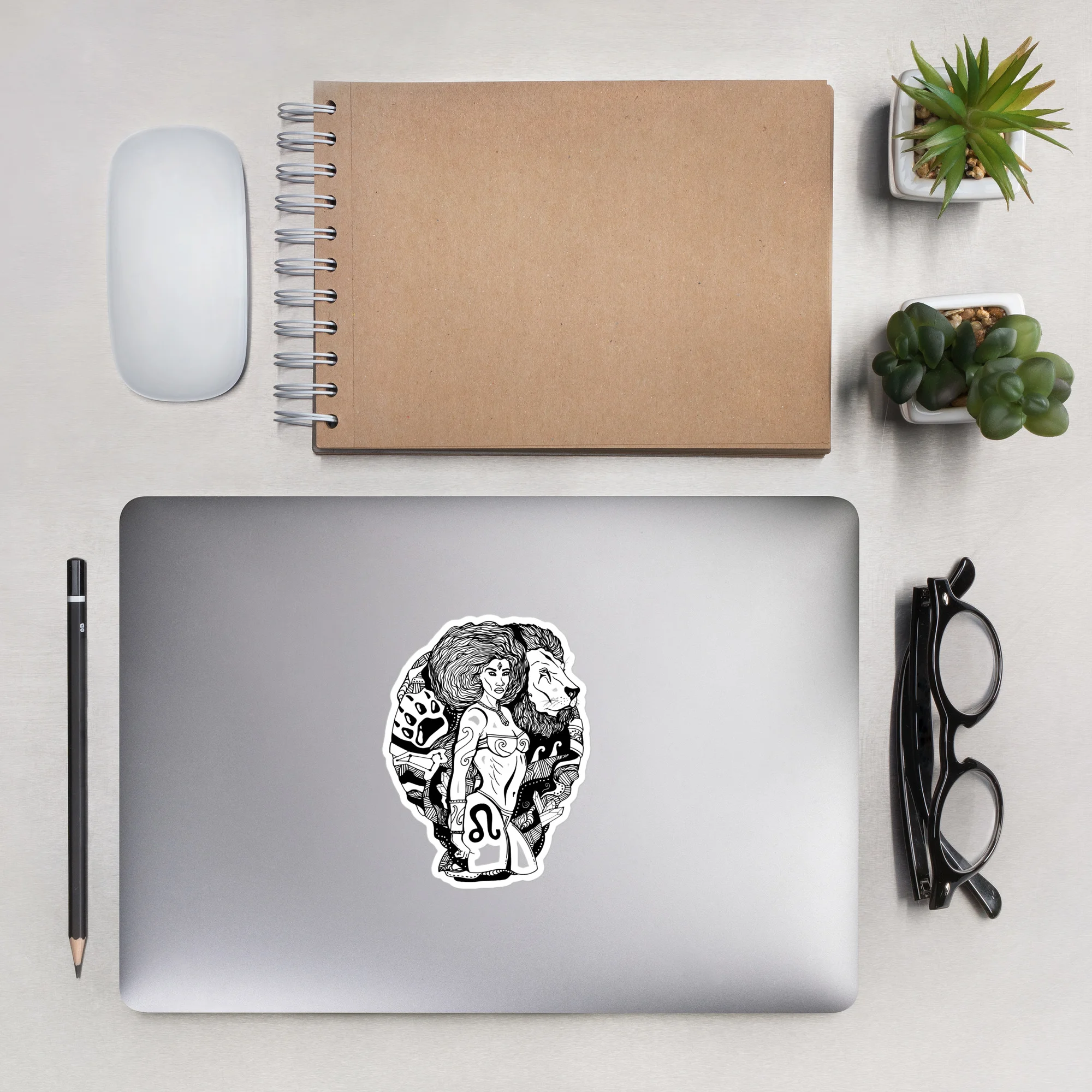 White kiss-cut Leo zodiac sticker with warrior woman and lion design on silver laptop.