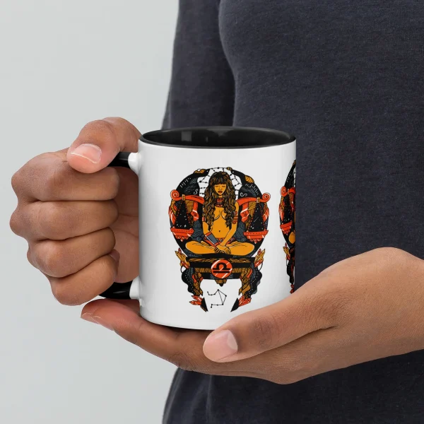Person holding a white libra zodiac coffee mug with orange and black artwork design and black interior rim