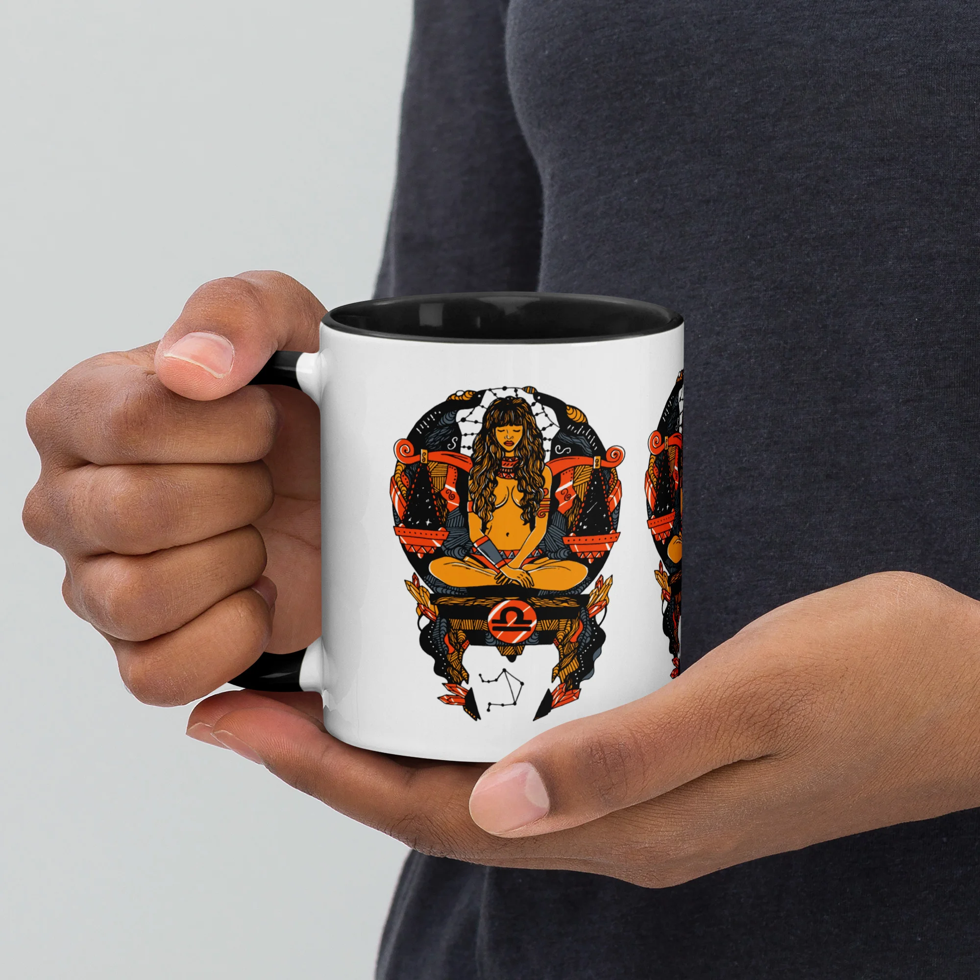 Person holding a white libra zodiac coffee mug with orange and black artwork design and black interior rim