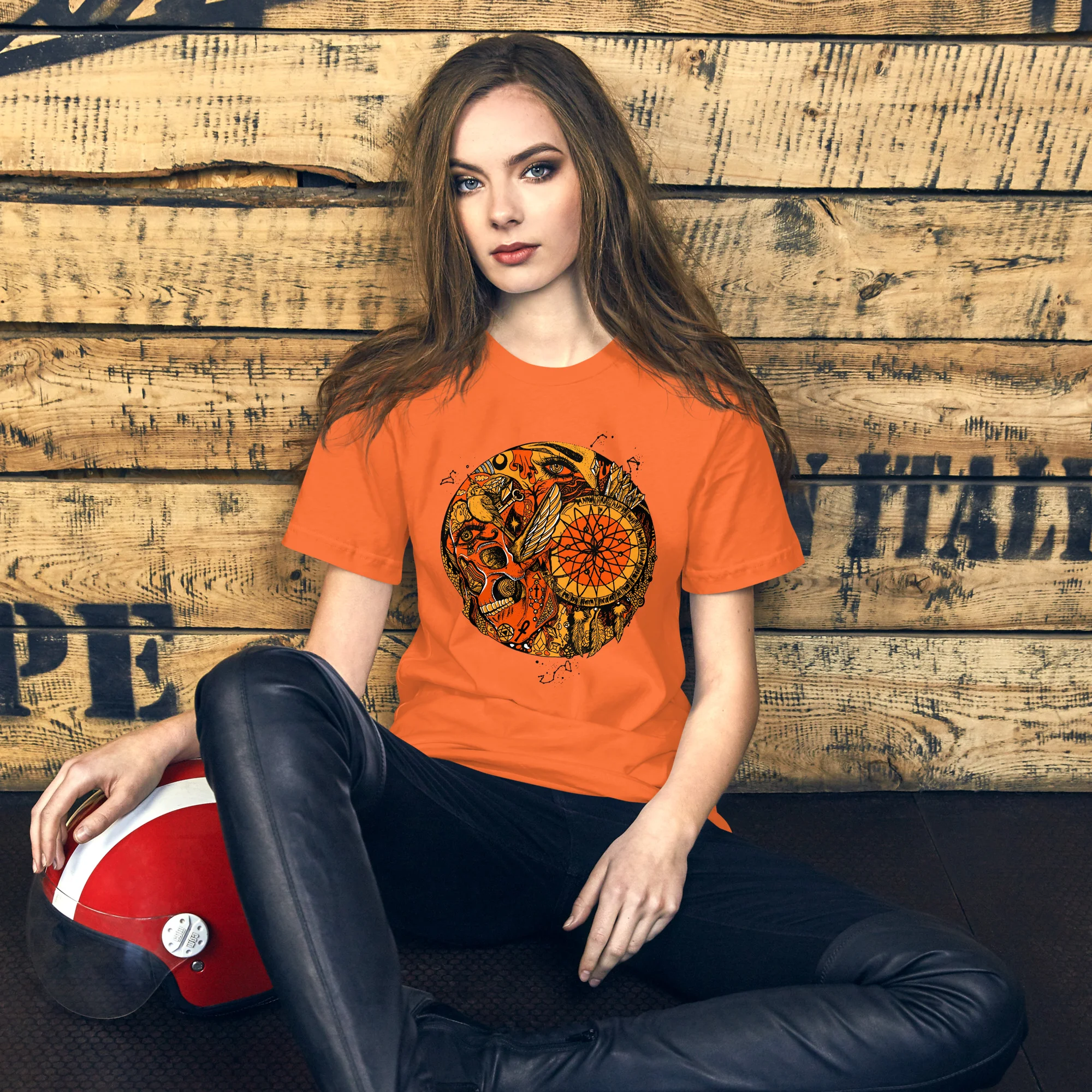 Woman wearing orange mystical skull graphic tshirt with intricate black design on wooden background