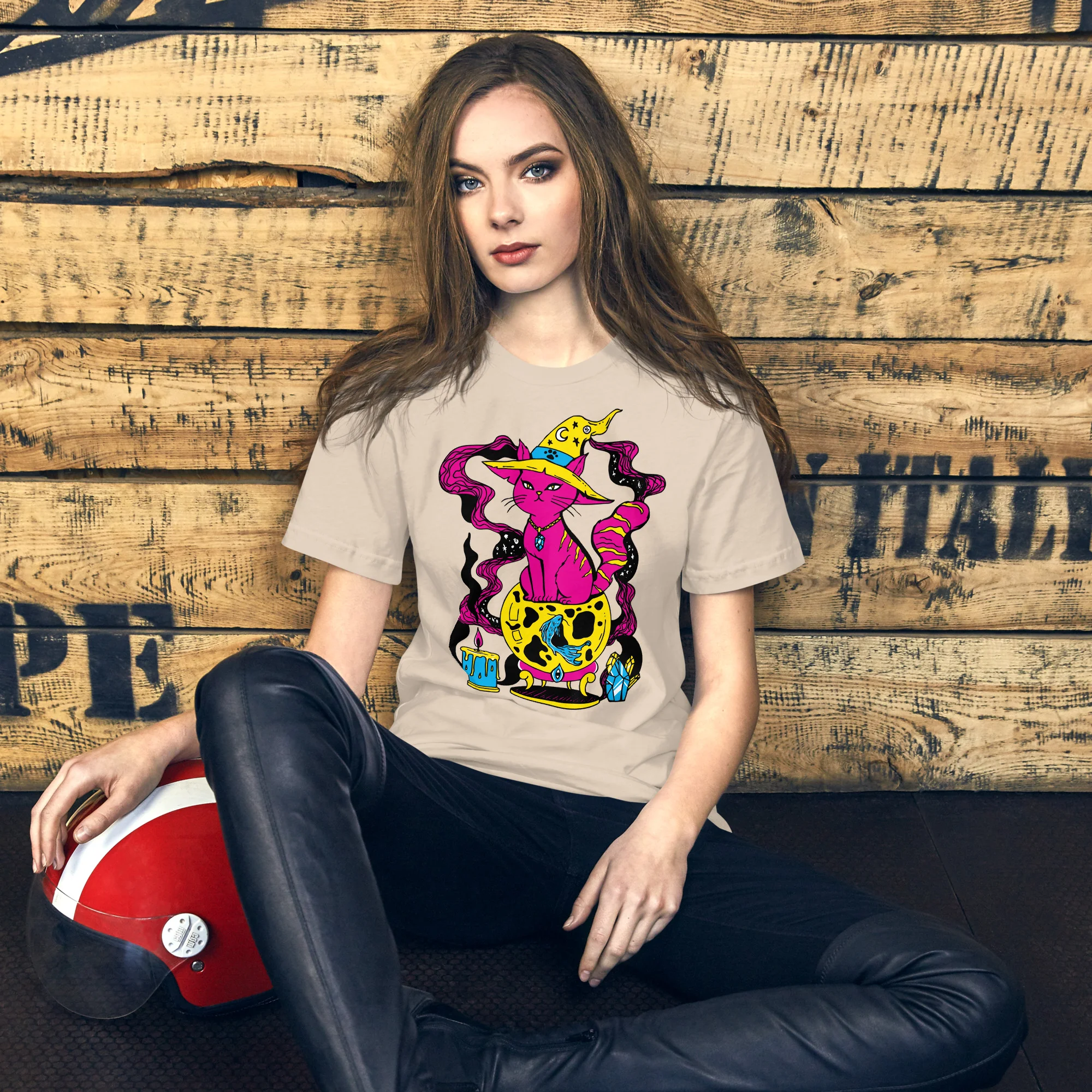 Woman wearing a cream pink cat t-shirt with a colorful magical fortune cat graphic design against a wooden backdrop
