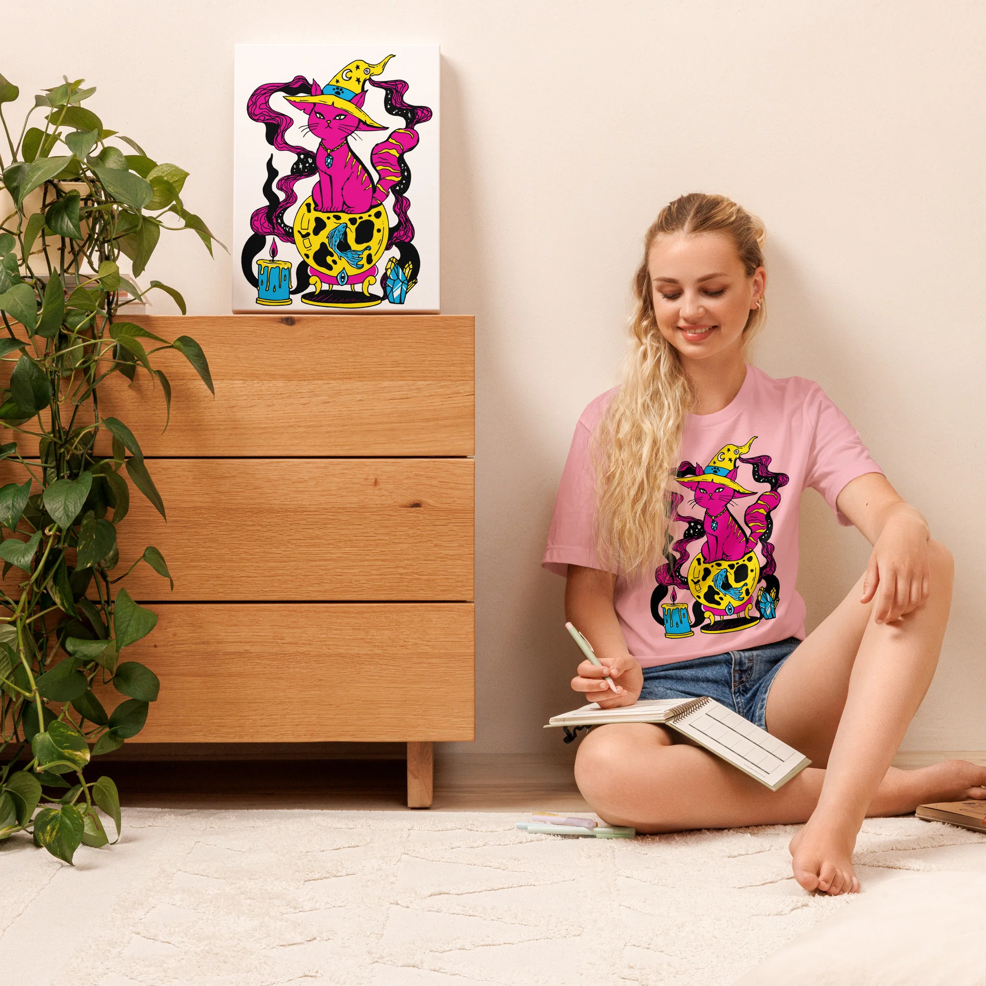 Woman wearing a pink cat t-shirt featuring a colorful magical fortune cat design with yellow hat and cosmic details