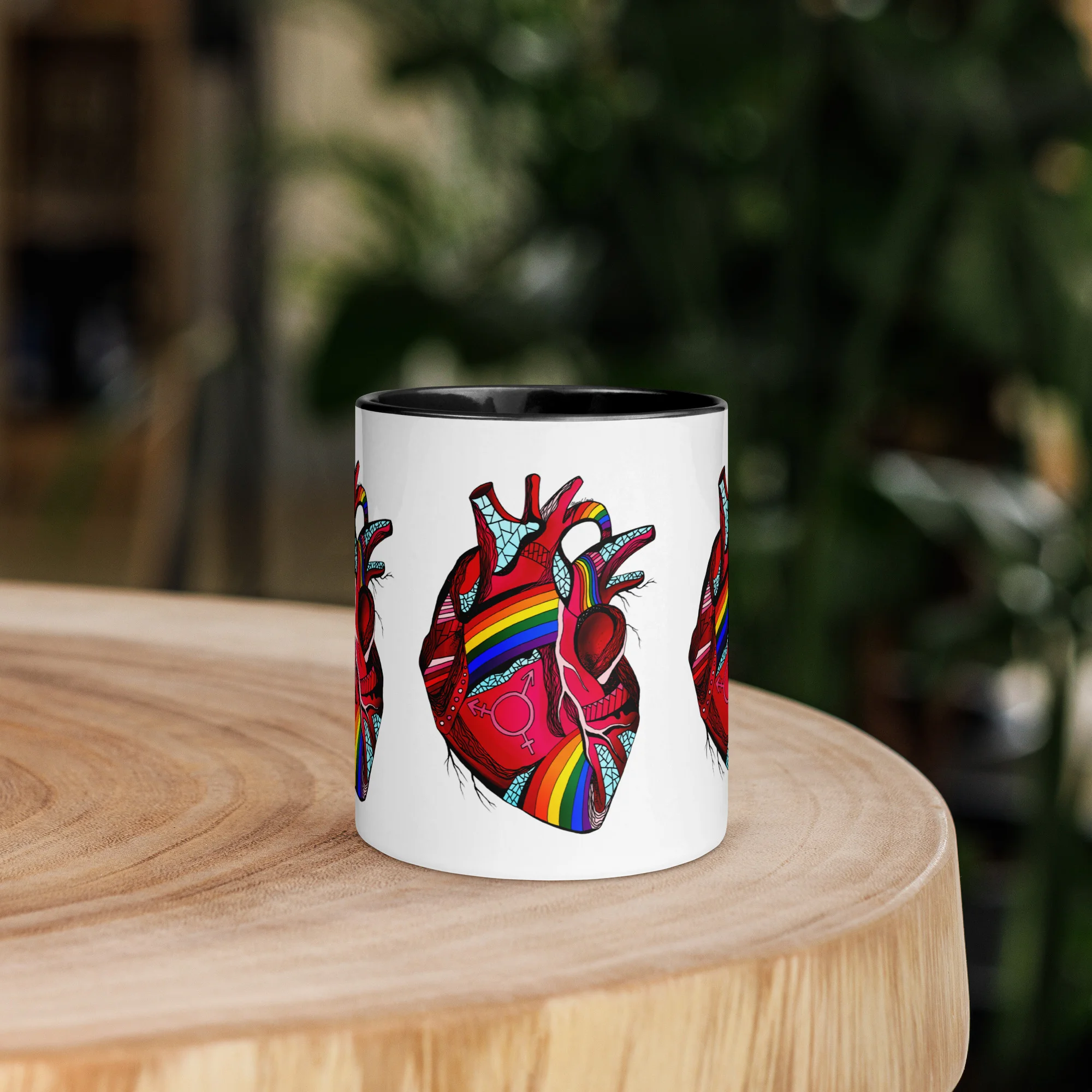 Colorful pride heart mug with white body, black rim, and rainbow anatomical heart design on wooden table