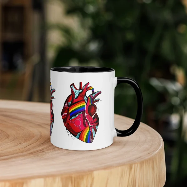 Colorful pride heart mug with rainbow design and black handle sitting on wooden table
