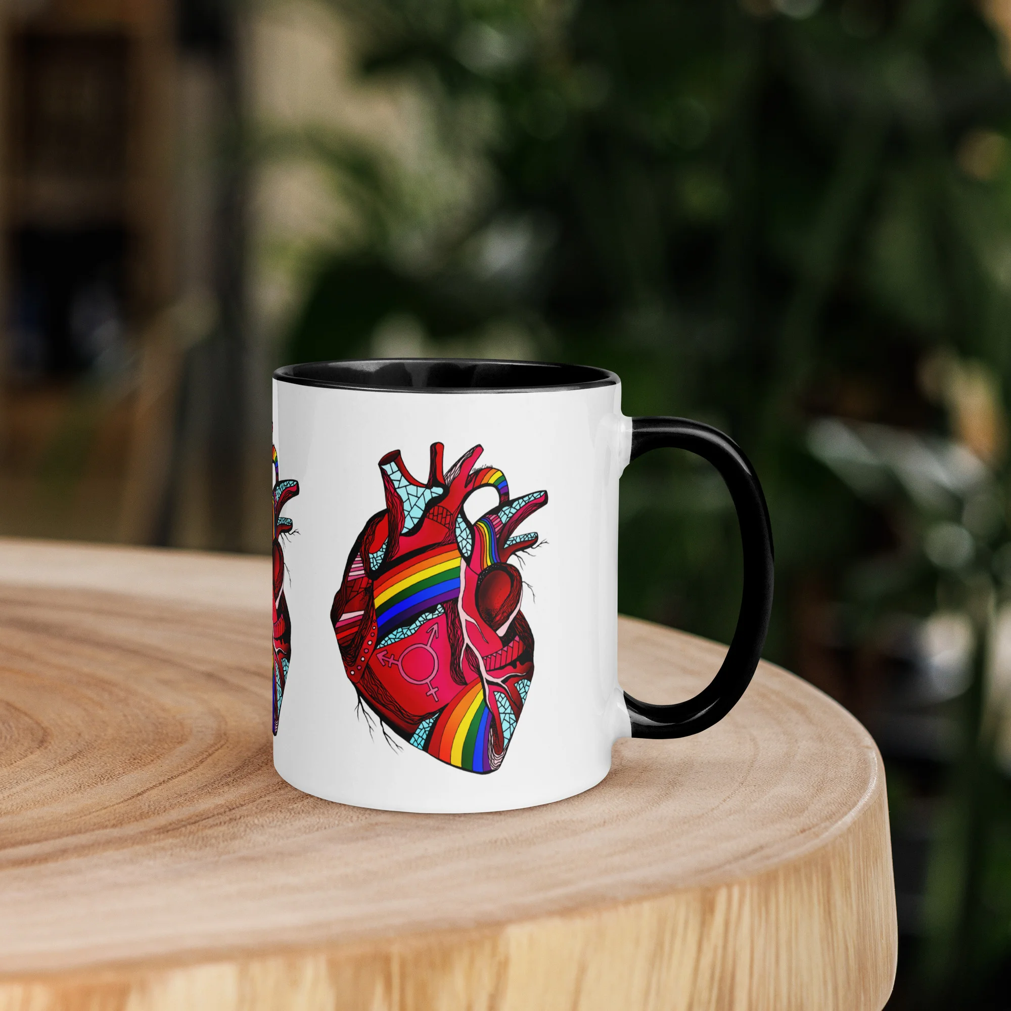 Colorful pride heart mug with rainbow design and black handle sitting on wooden table