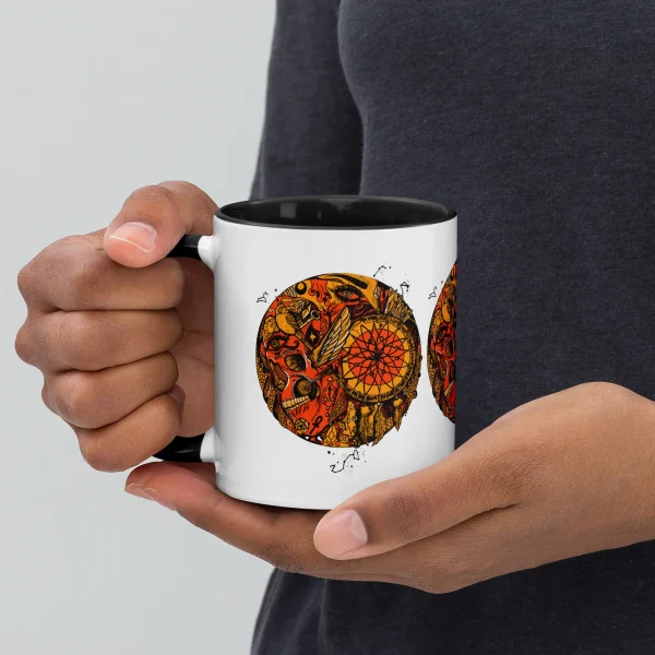 Person holding a white skull coffee mug with orange and black gothic artwork design and black interior rim
